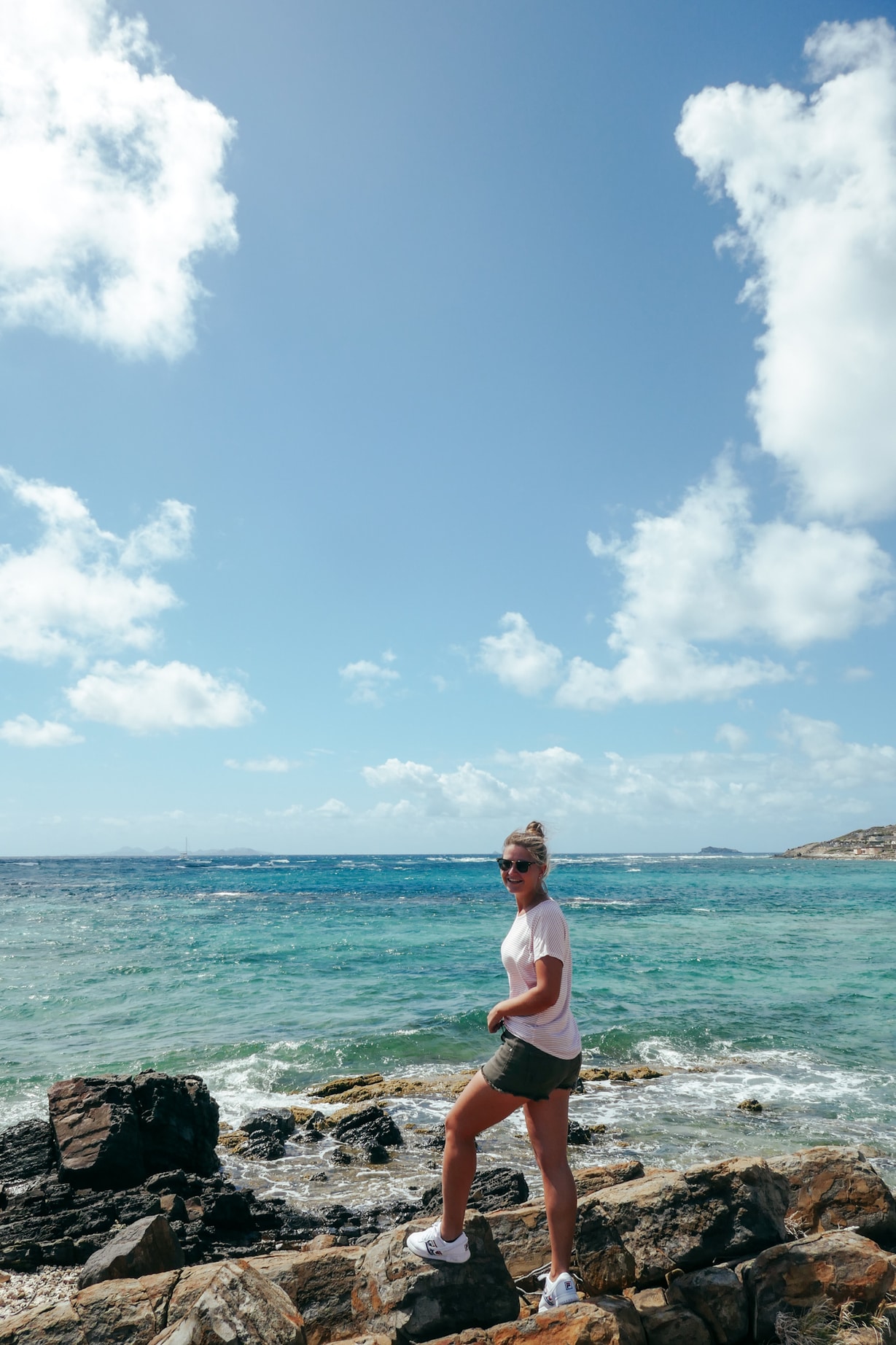 A young woman standing on rocks over the ocean smiling at the camera in Sint Maarten