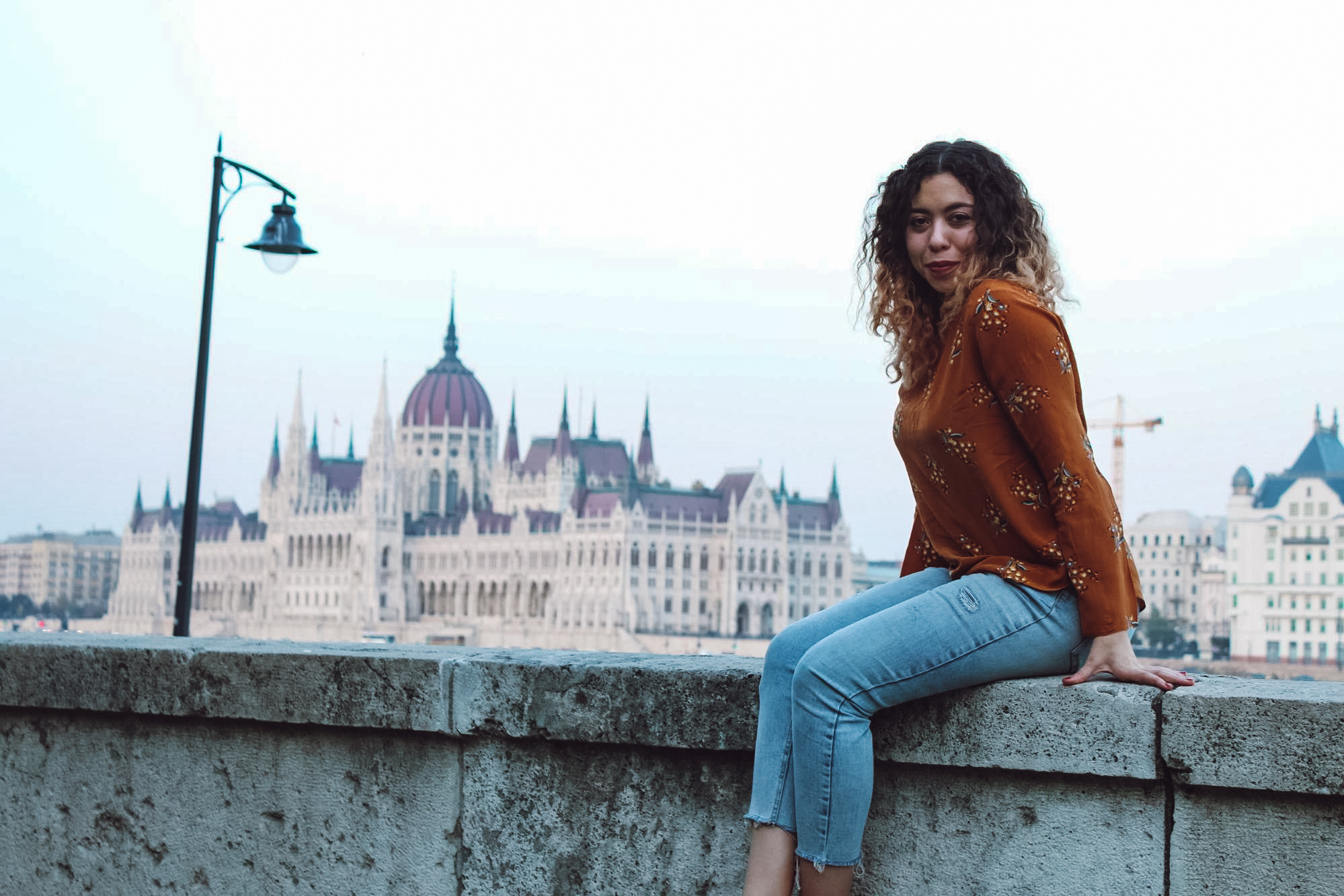 Woman sitting on ledge in Budapest with Parliment building in the background