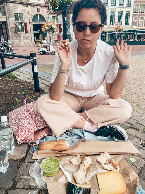 A woman having a picnic on the cobblestone eating gouda cheese in Gouda