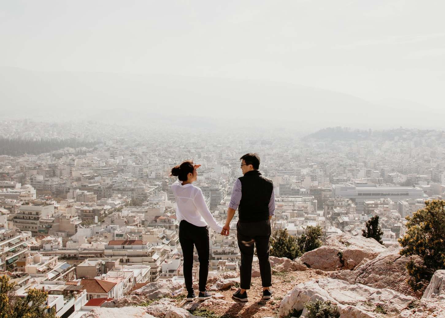 A couple, holding hands, overlooking a city from a look out point
