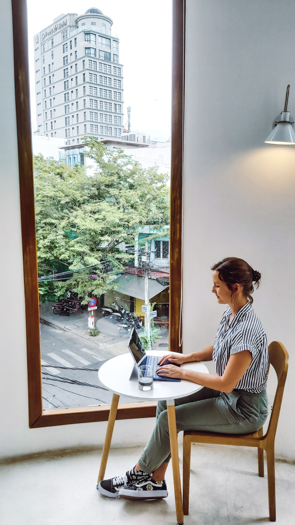 A woman working on a laptop in front of a window displaying a street in Da Nang, Vietnam