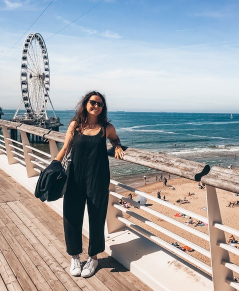 Woman enjoying summer in Scheveningen Beach at The Hague standing on a boardwalk with a ferris wheel and beach in the background
