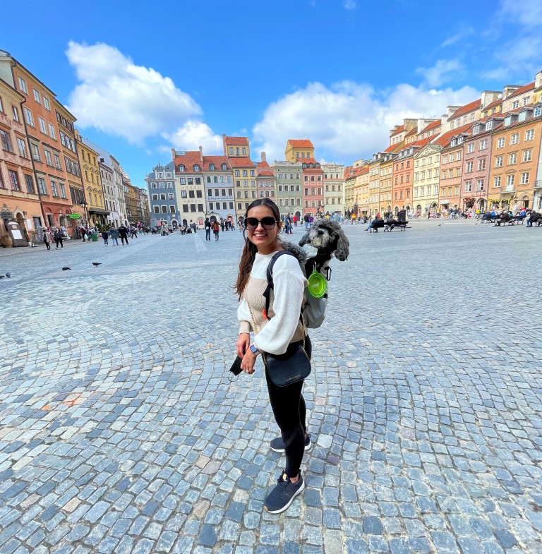 a female expat from the USA now living in Poland standing in the Warsaw square with her dog in a backpack on her back