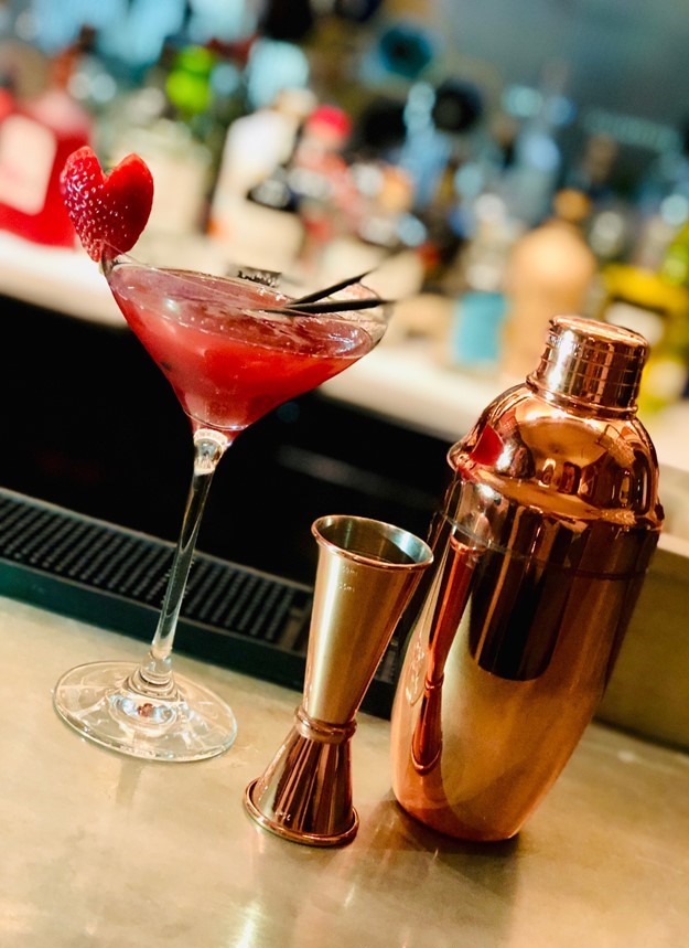 Copper barware sitting next to a delicious looking valentine's themed cocktail with strawberry garnish.