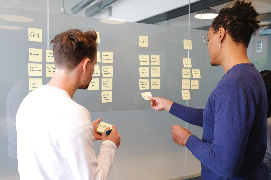 two men discussing while holding a sticky note