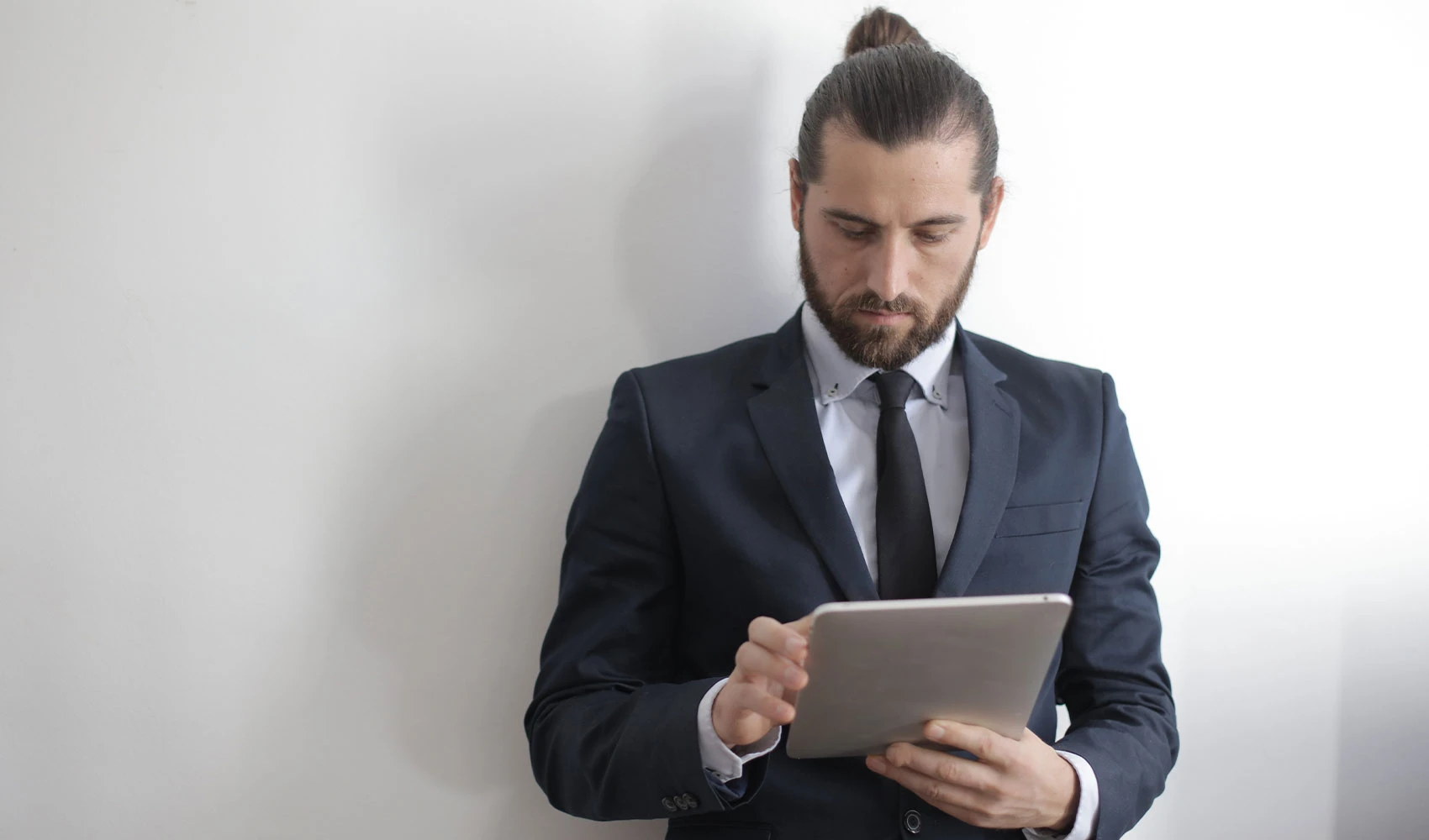 Bearded man with man bun wearing business attire while using iPad