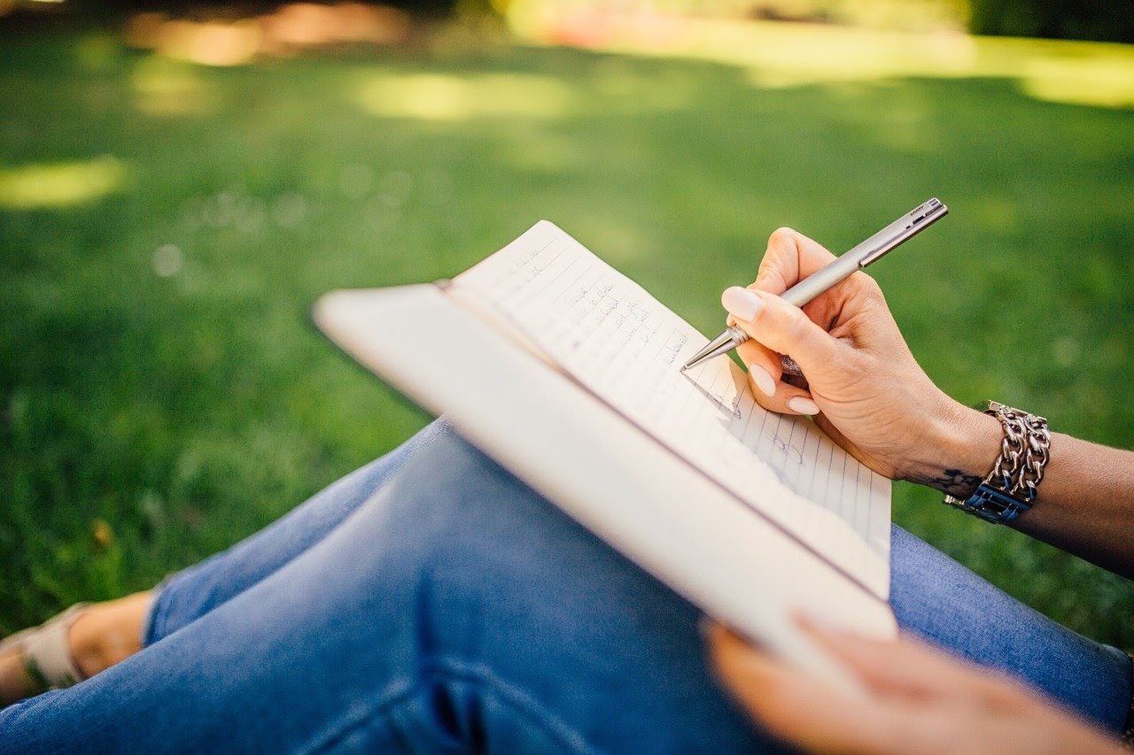 A content creator sits in the grass and journals after gaining new content inspiration