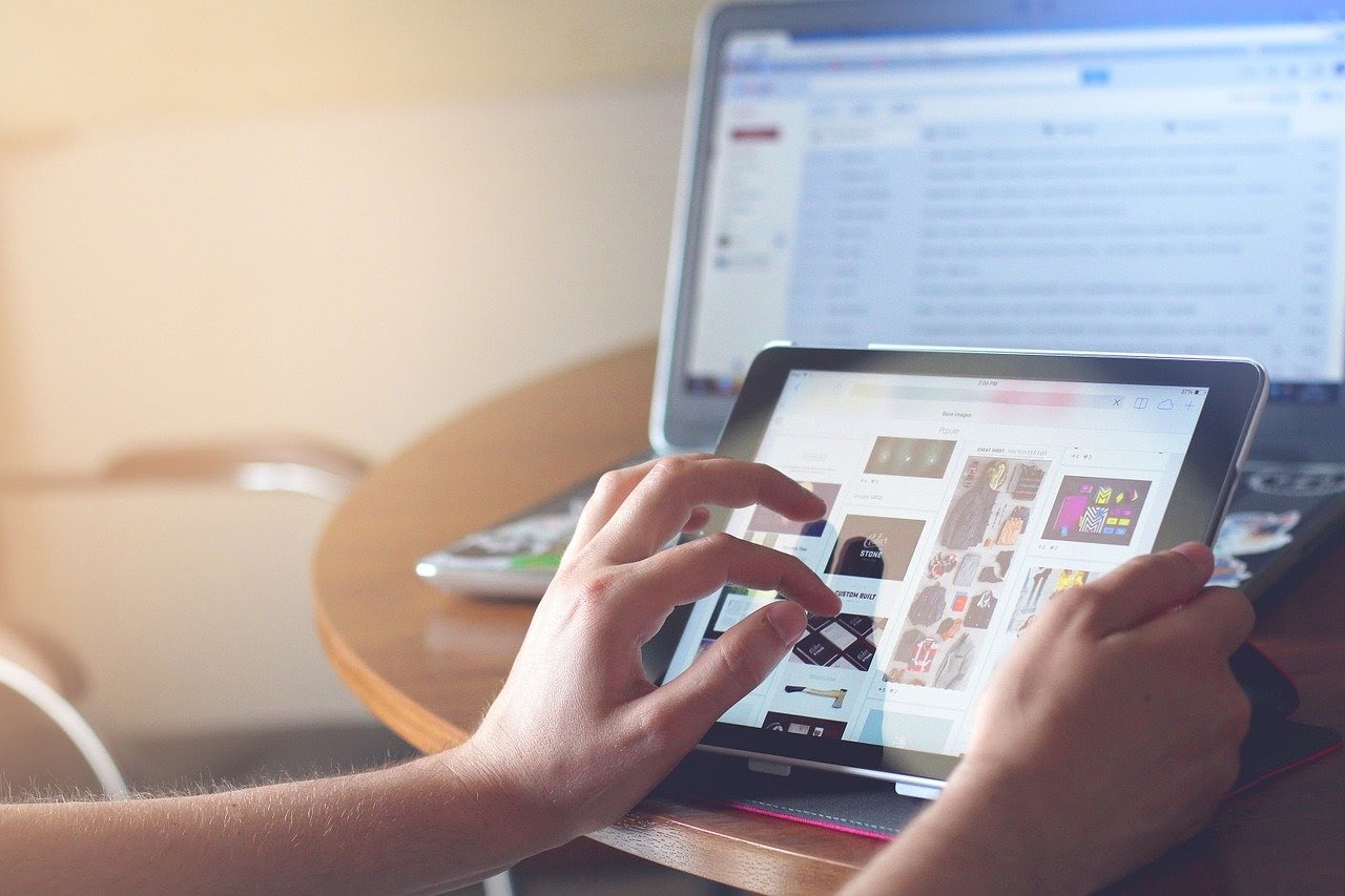 A businessperson looks at their tablet in the foreground, while the email blasts on their laptop in the background go unnoticed