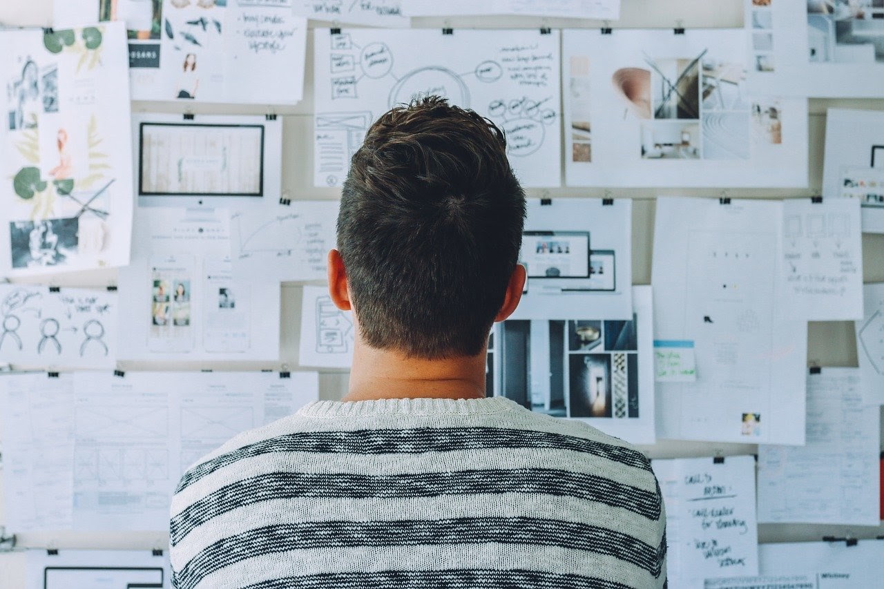 An email blast can be improved with quality design, pictured here by a man looking at a wall with different images and design concepts