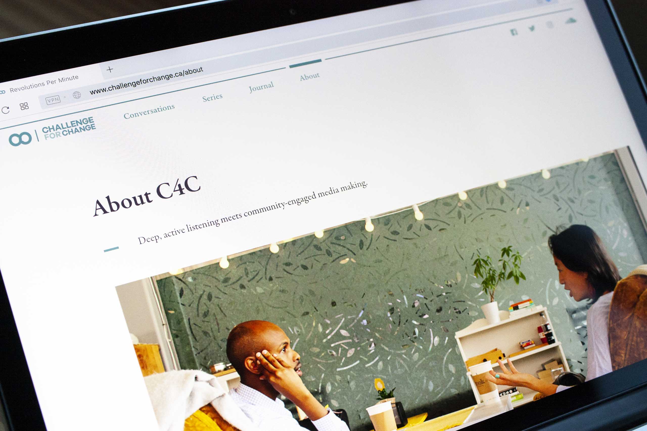 Photograph of a laptop screen with the about page of the challenge for change website with a large image of two people engaged in conversation — by Yagnyuk.