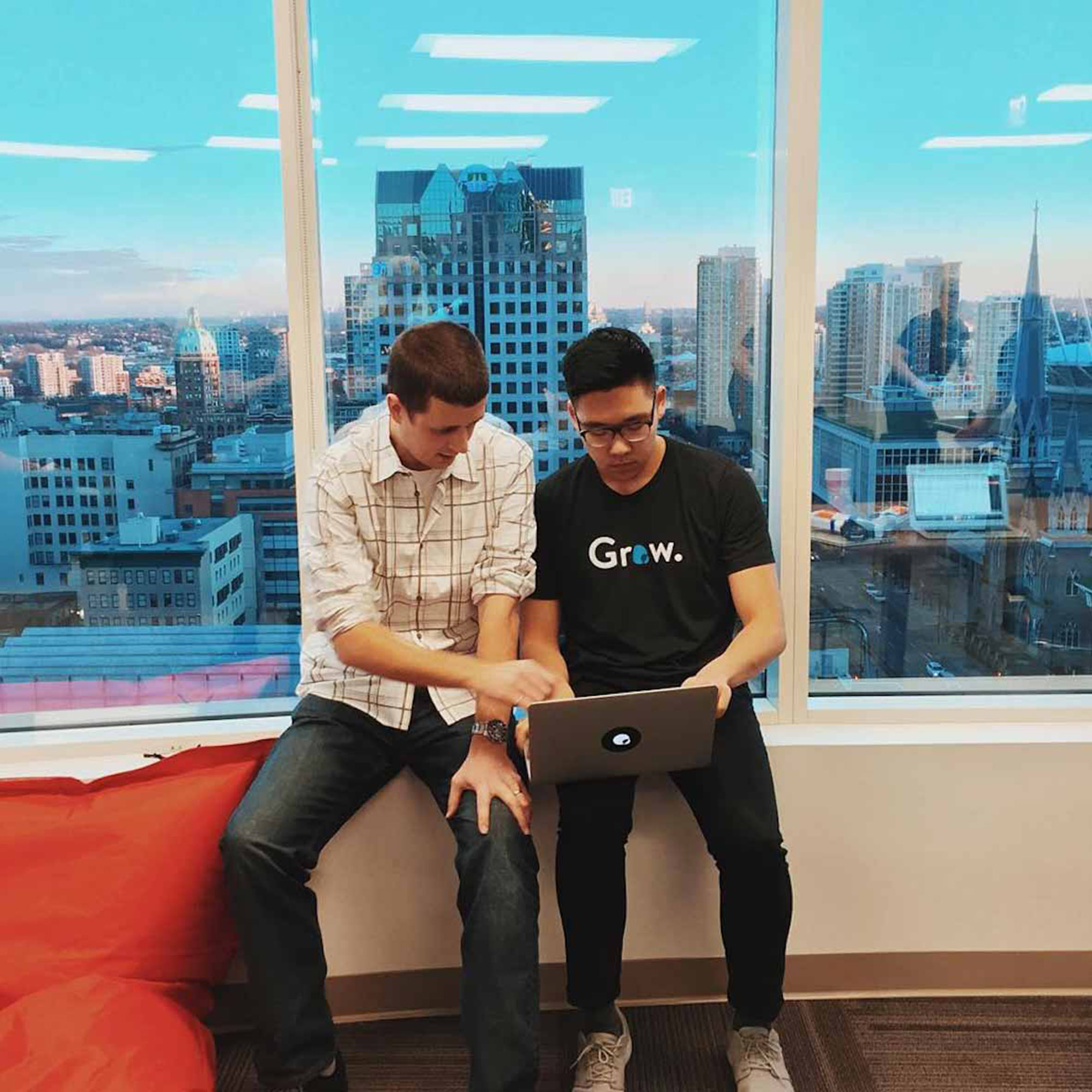 Team members by a window wearing branded shirts, with branded stickers on the laptop — by Yagnyuk.