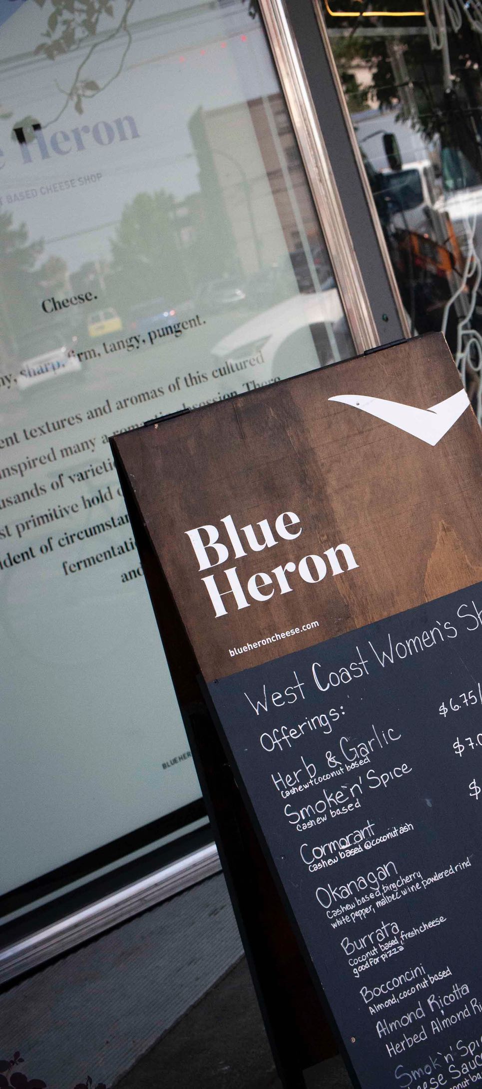 Blue Heron Storefront with store windows featuring a handsigned brand manifesto with branding applied to a sandwich board placed next to it — by Dima Yagnyuk.