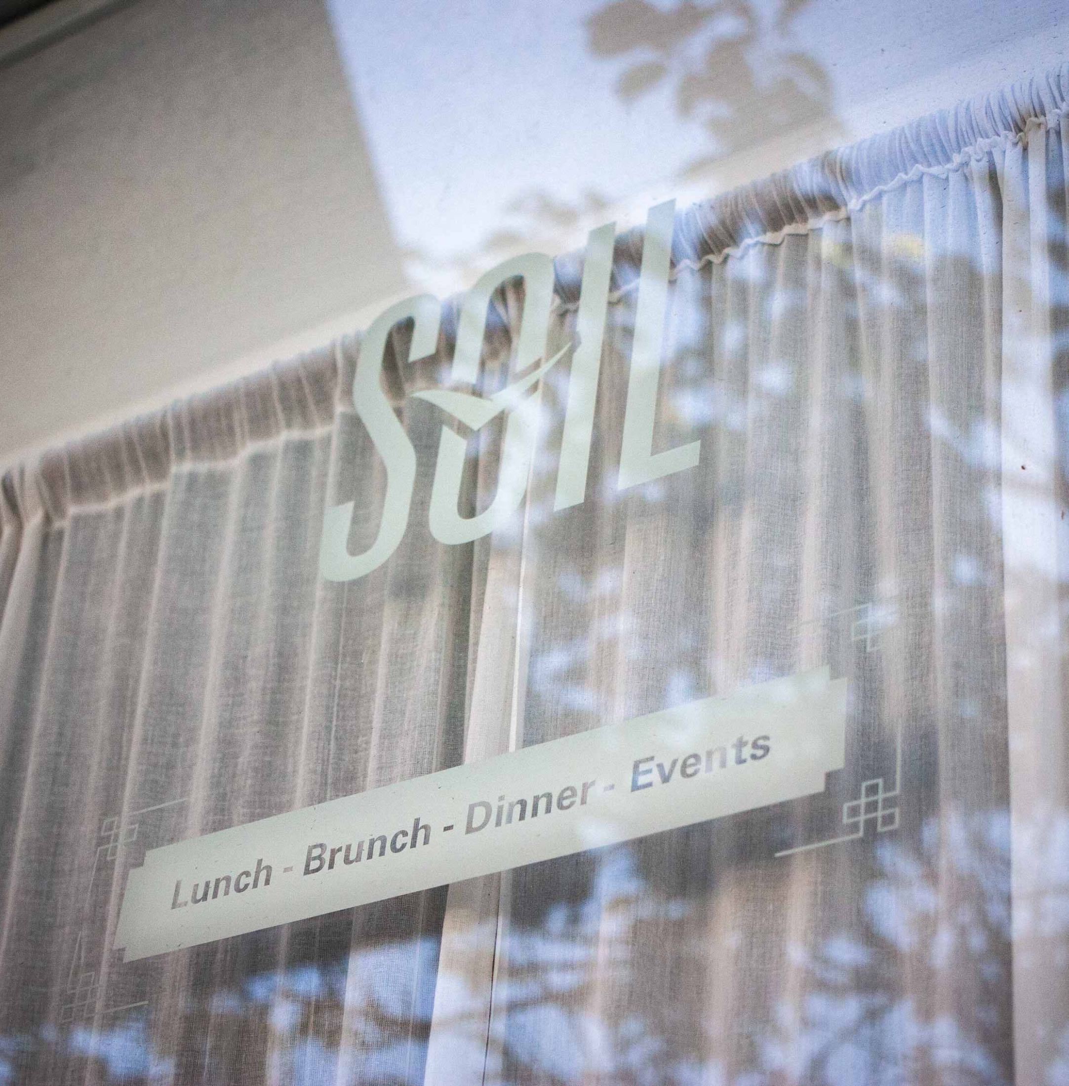 Soil Restaurant window close up featuring the logo in front curtained interior — by Dima Yagnyuk.