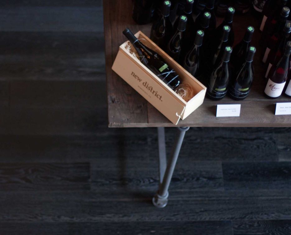 New District wine store interior setup showcasing table with branded packaging next to wine display — by Yagnyuk.