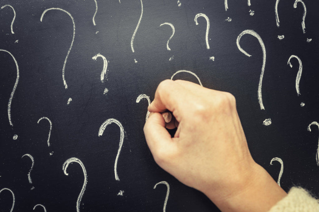 a person writing question marks on blackboard