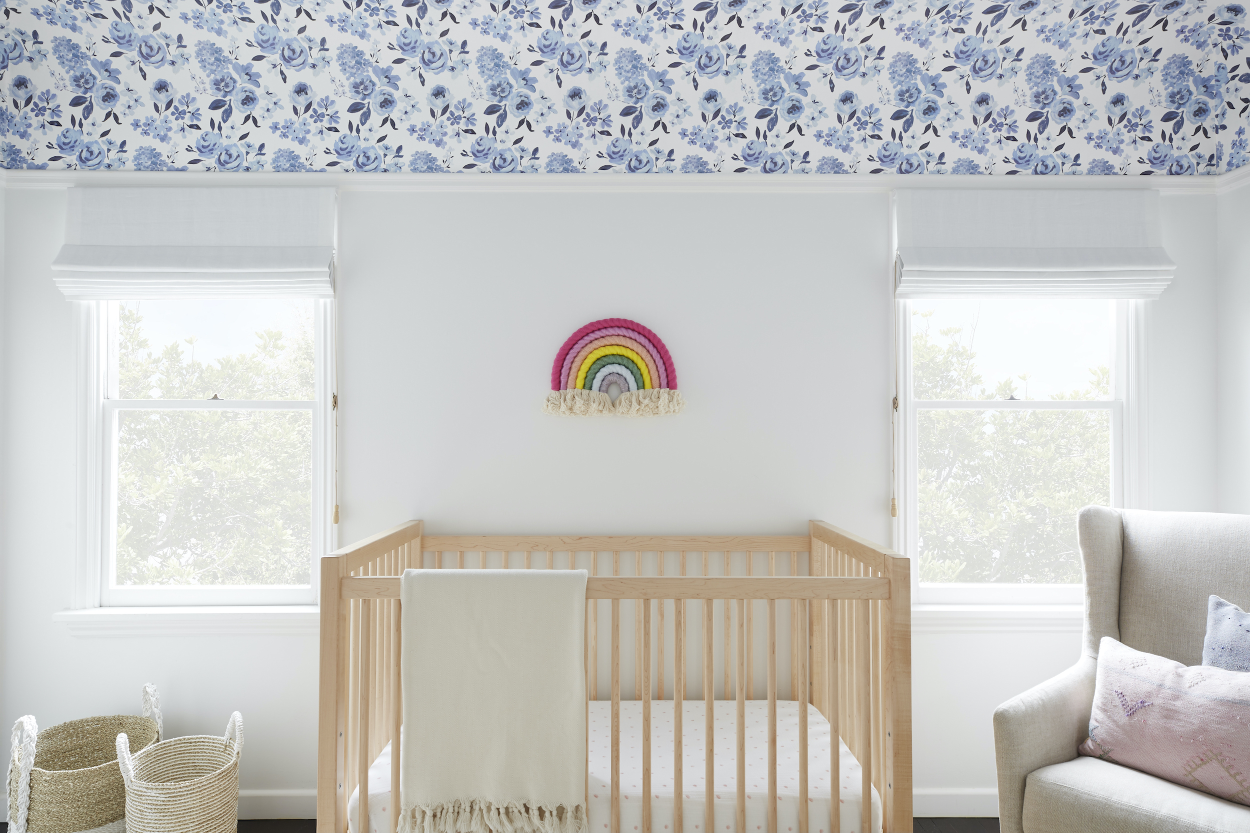 Roman shades mounted outside two windows will block light from shining on the crib between them