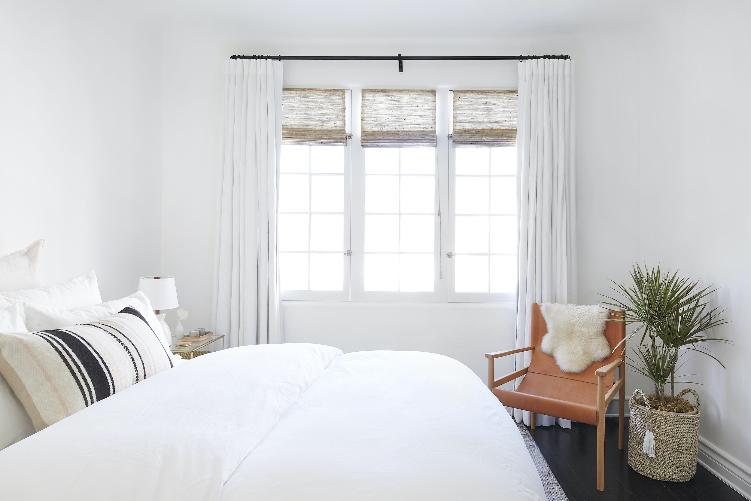 Everhem’s linen drapes and woven woods cover three side-by-side windows in a neutral-theme bedroom