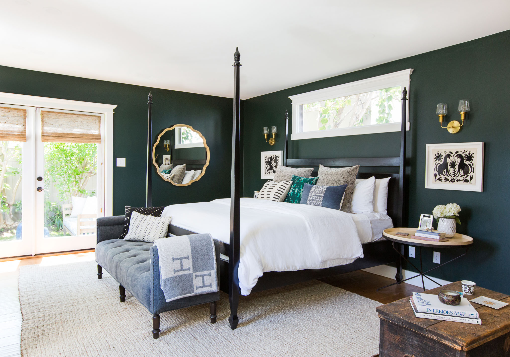 A master suite with four-poster bed, rich-toned walls and woven wood shades