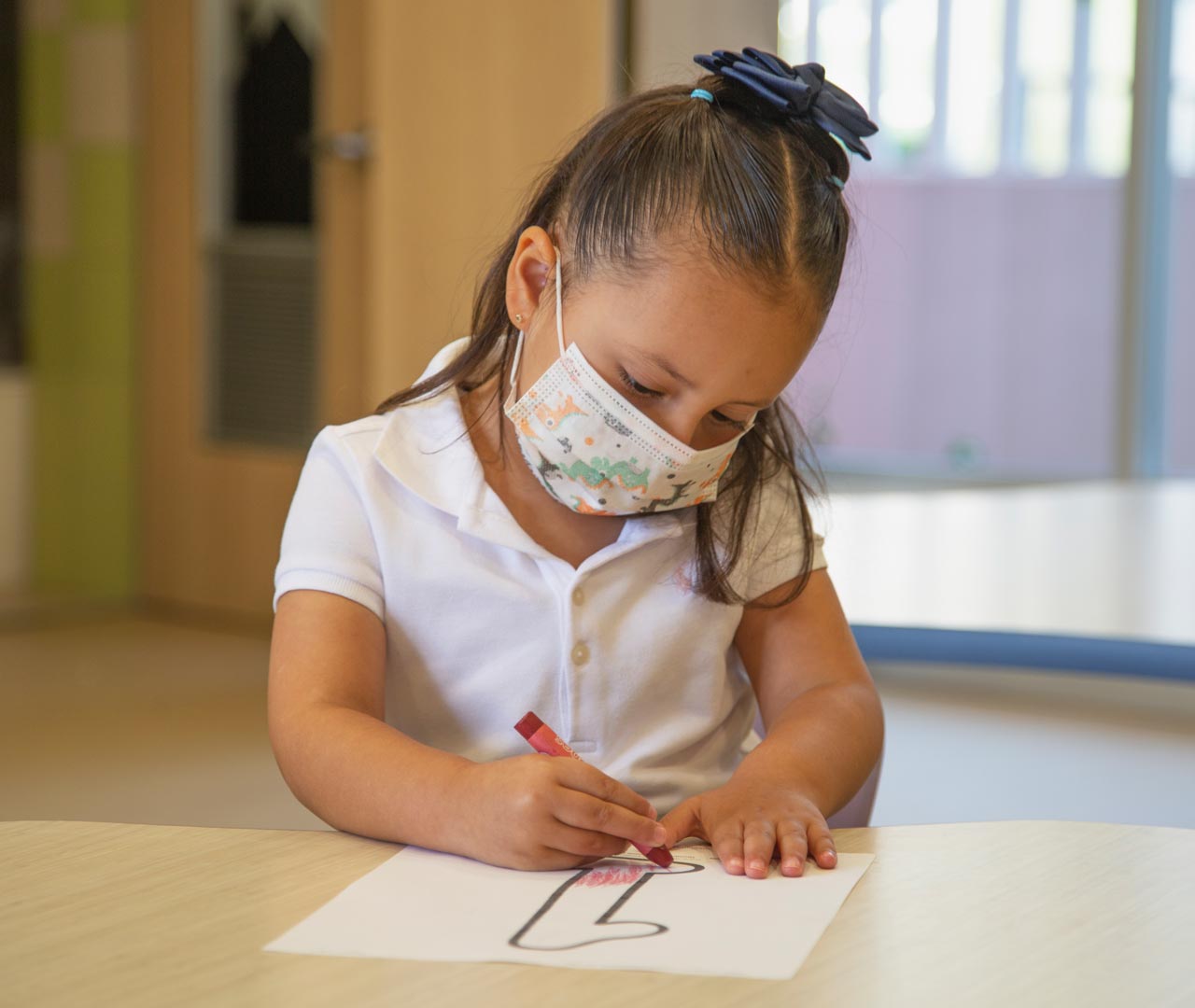 Alumna de preescolar coloreando un dibujo mientras utiliza un cubrebocas.