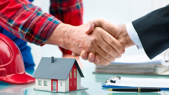 Two hands shaking over a table with a model house, pen, and documents.