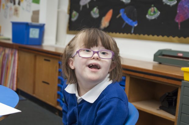 A little girl in her uniform in a special school smiling at the camera.