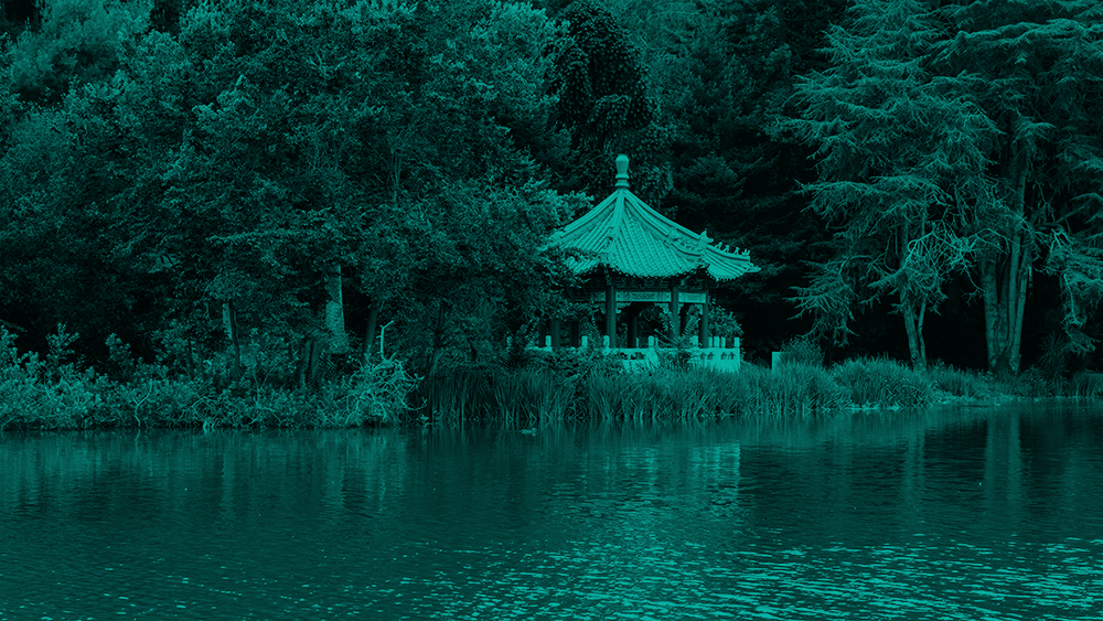 A pagoda sits at the edge of Stow Lake, surrounded by trees. There are tall grasses at the water's edge that obsure the bottom of the pagoda.