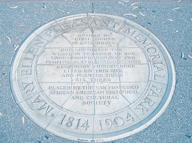 Photo of a round plaque embedded in a sidewalk - the plaque reads "Mary Ellen Pleasant Memorial Park 1814 - 1904" around the outside rim. The inside of the circle reads: "Mother of civil rights in Californai. She supported the western terminus of the underground railway for the fugitive slaves 1850-1865. This legendary pioneer once lived on this site and planted these six trees. Placed by the San Francisco African American Historical and Cultural Society."