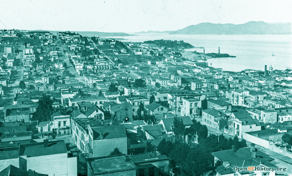 An aerial view overlooking clustered wooden buildings on Telegraph Hill towards the SF bay and Marin headleands