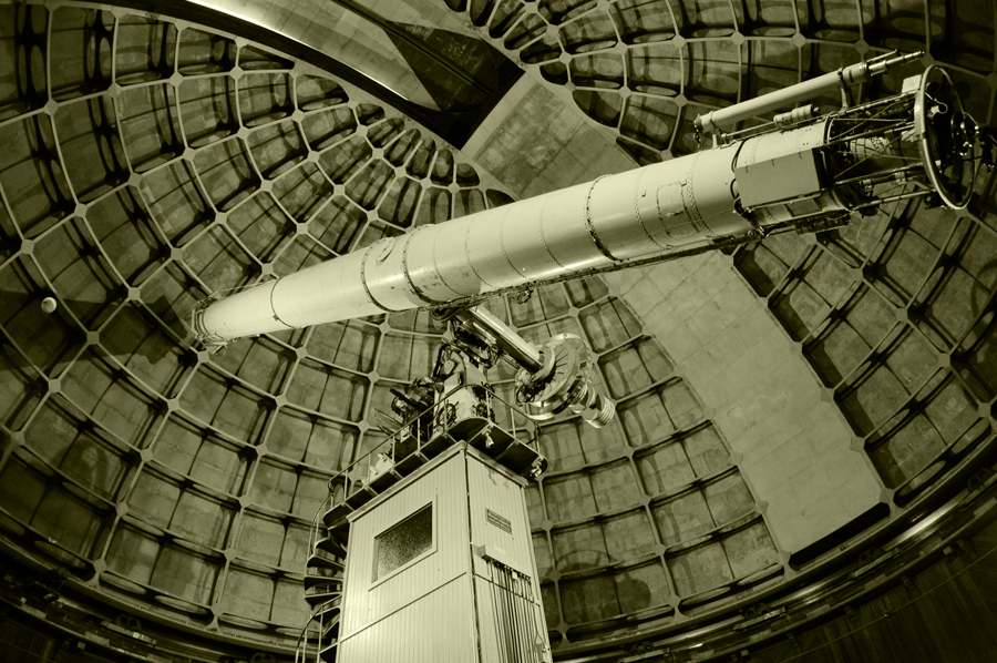 A photo of the telescope, shot from the floor looking up. Behind the telescope is the gridded internal structure of the domed roof