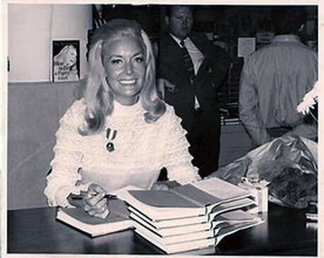 Pat at a book signing for "How to Be a Party Girl." She's smiling wide as she signs books, and her hair looks extremely 1960's