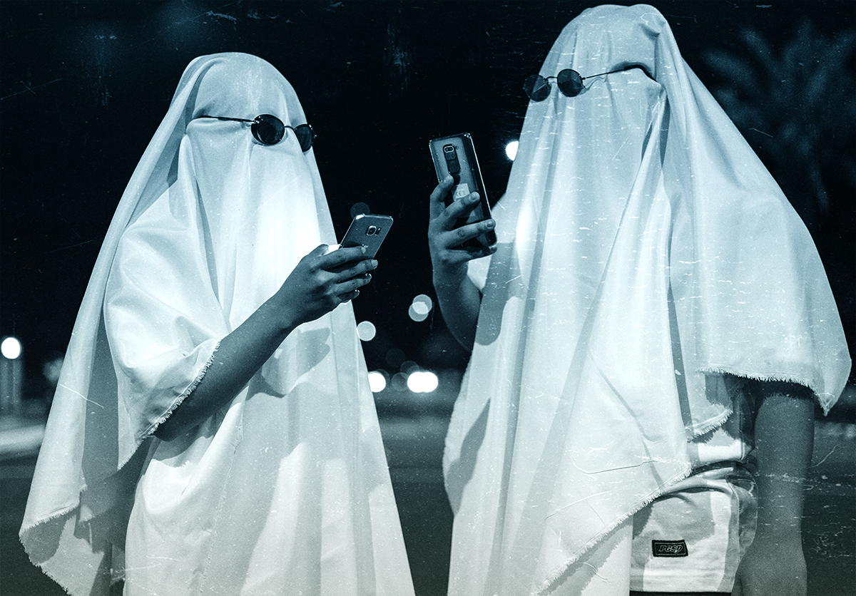 Two people dressed as ghosts (literally just wearing a sheet over their heads) wearing sunglasses and holding up cell phones as if they are looking at them.
