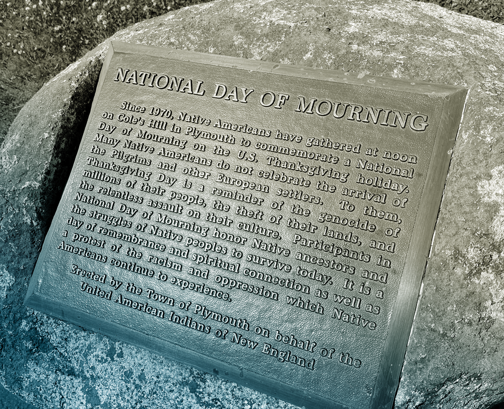 A closeup of the plaque describing the National Day of Mourning. The inscription reads, “Since 1970, Native Americans have gathered at noon on Cole’s Hill in Plymouth to commemorate a National Day of Mourning on the U.S. Thanksgiving holiday. Many Native Americans do not celebrate the arrival of the Pilgrims and other European settlers. To them, Thanksgiving Day is a reminder of the genocide of millions of their people, the theft of their lands, and the relentless assualt on their culture. Participants in National Day of Mourning honor Native ancestors and the struggles of Native peoples to survive today. It is a day of remembrance and spiritual connection as well as a protest of the racism and oppression which Native Americans continue to experience. Erected by the Town of Plymouth on behalf of the United American Indians of New England.”