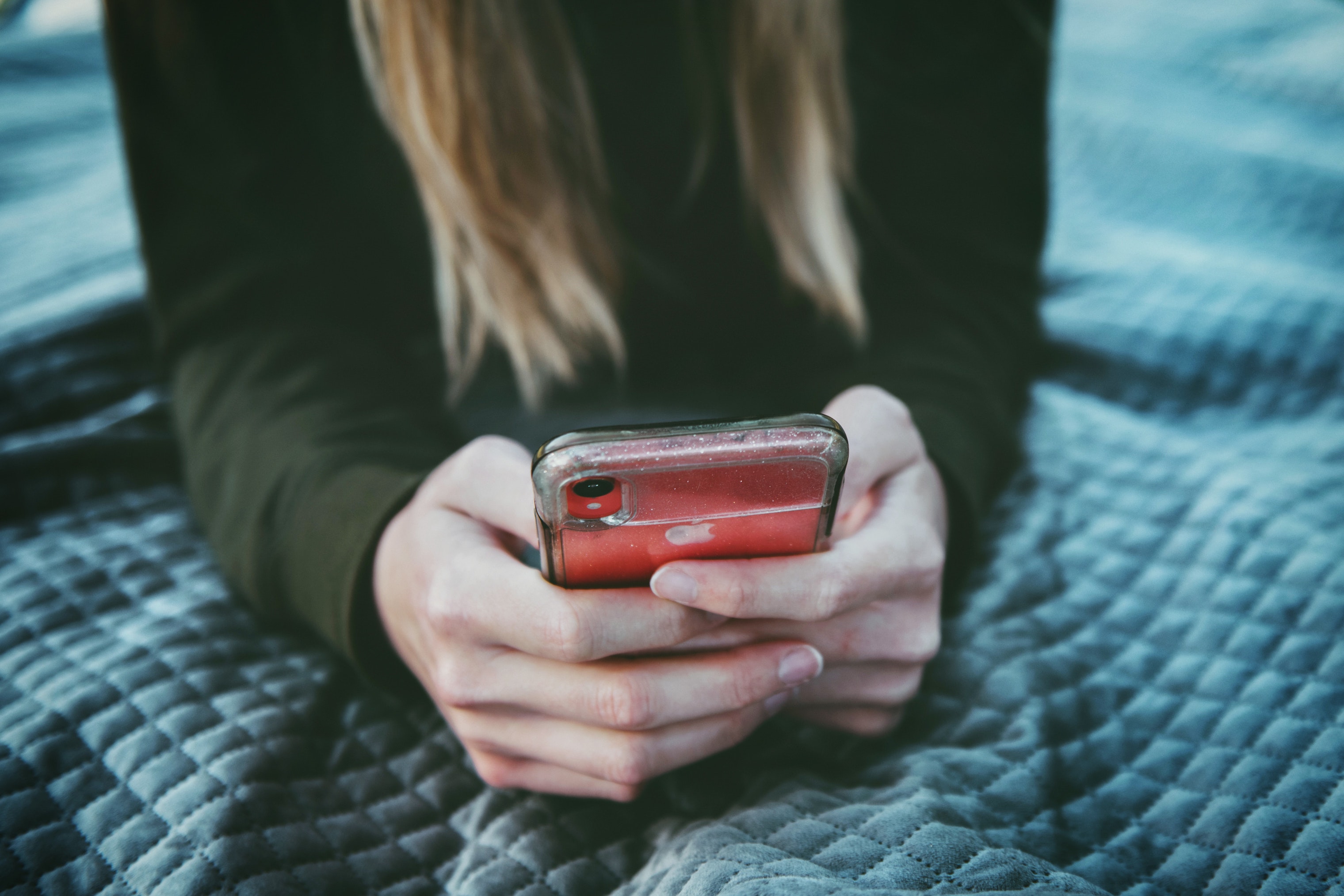 Image in blue tones of a blonde woman's hands holding a red iPhone.