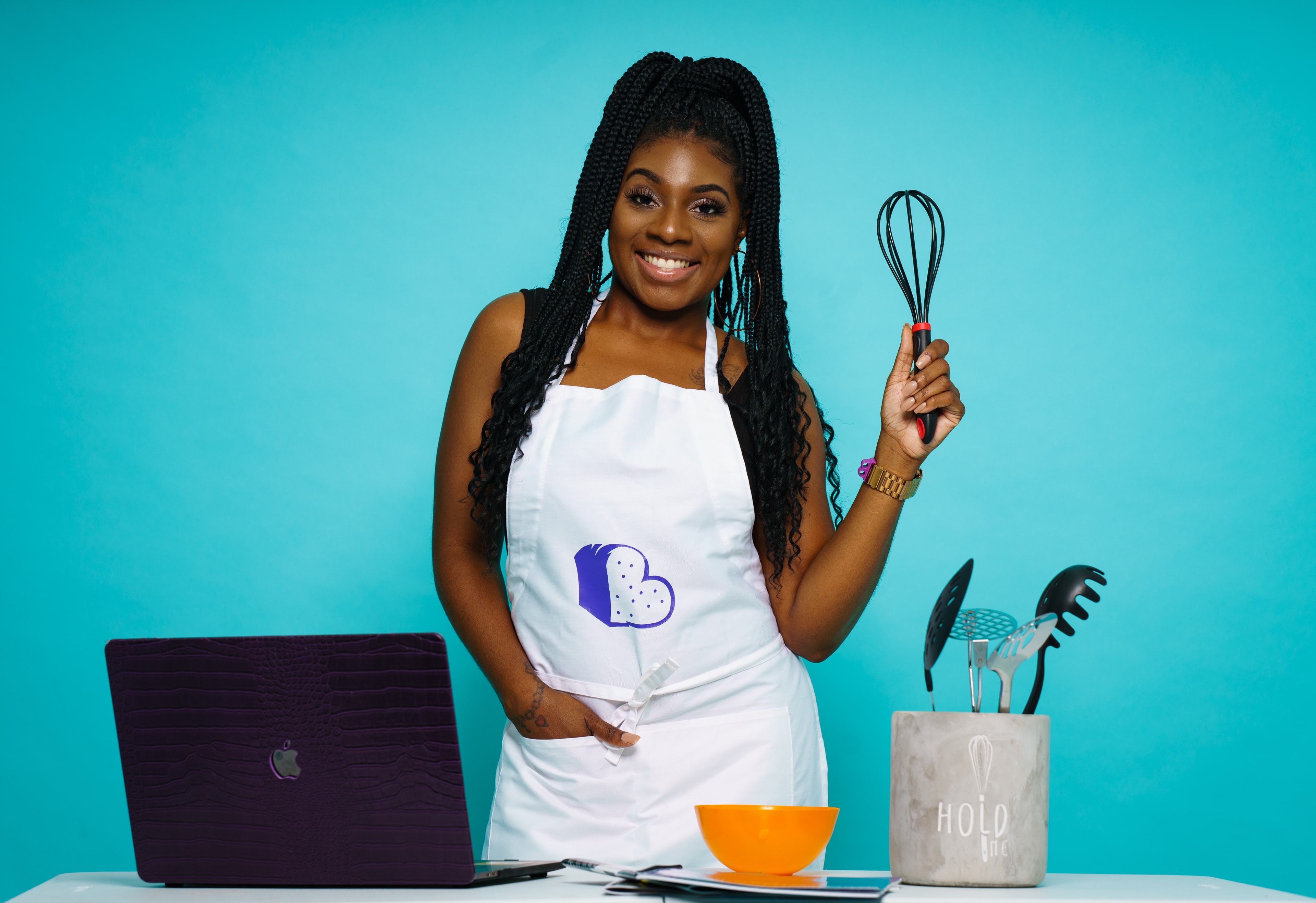 Woman wearing an apron, holding a whisk in front of a blue background
