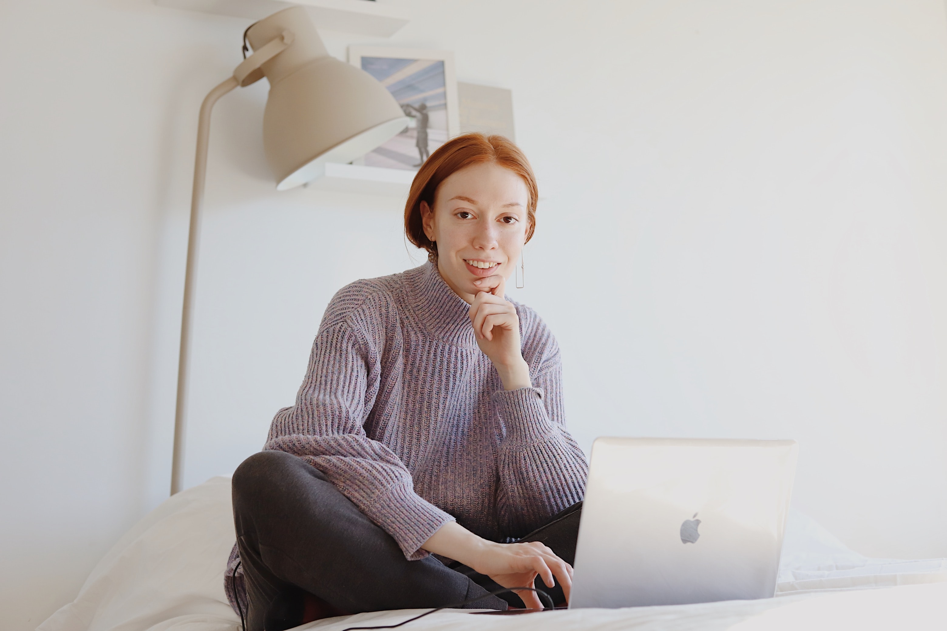 Image of woman sitting on a white bed with a laptop