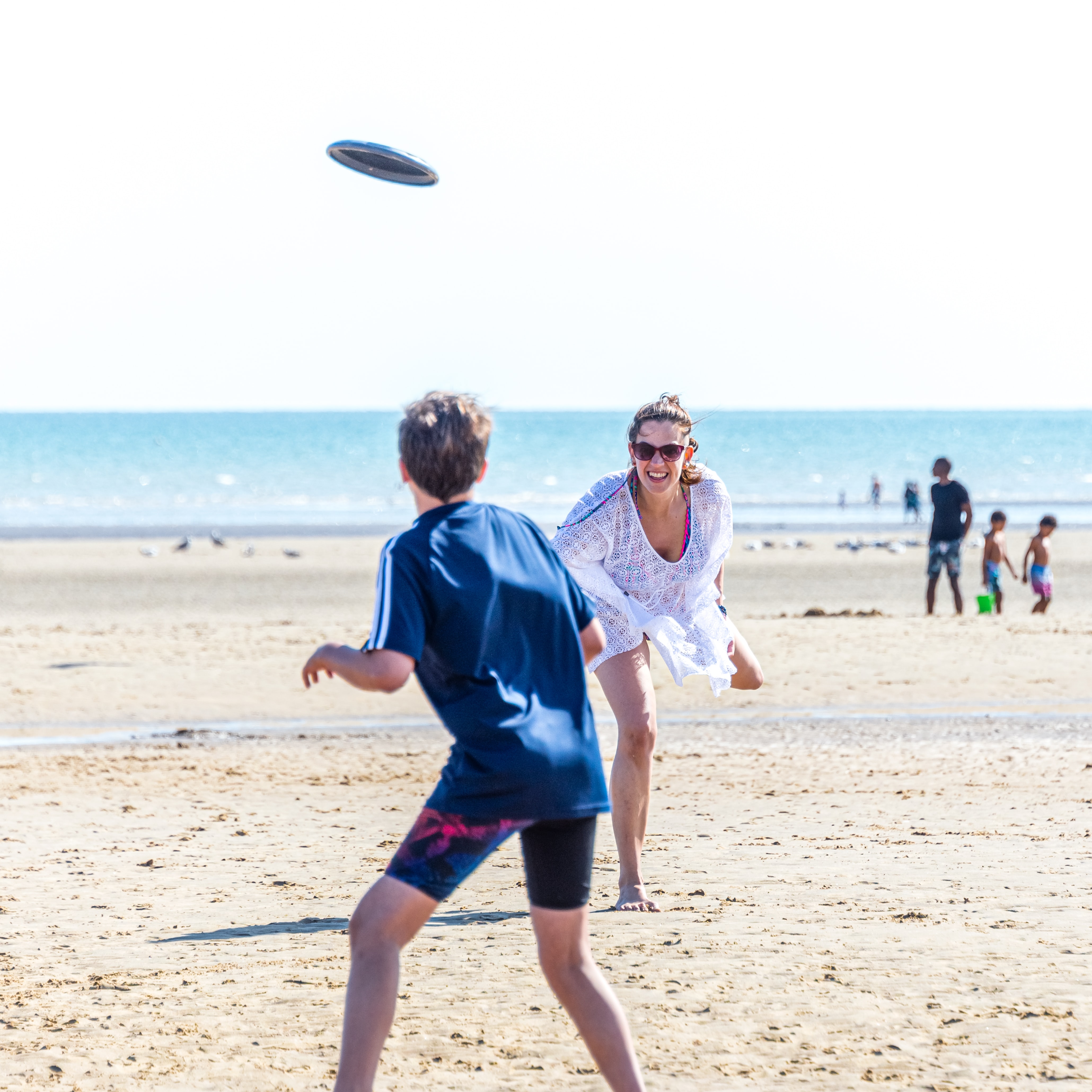 Woman plays frisbee on beach with teenage boy