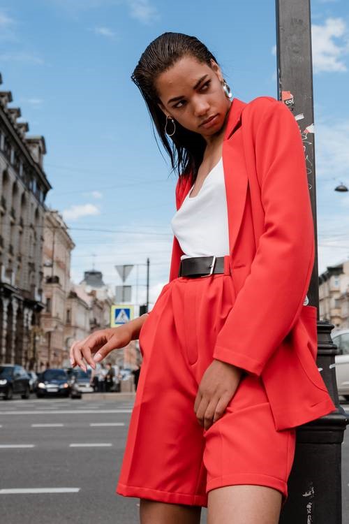 A girl in a red blazer leaning against a lamp post.