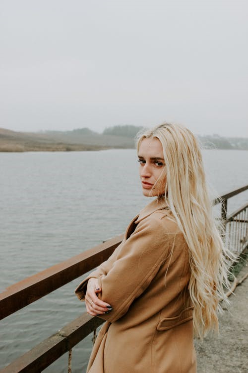 A woman in a brown coat standing near the water.