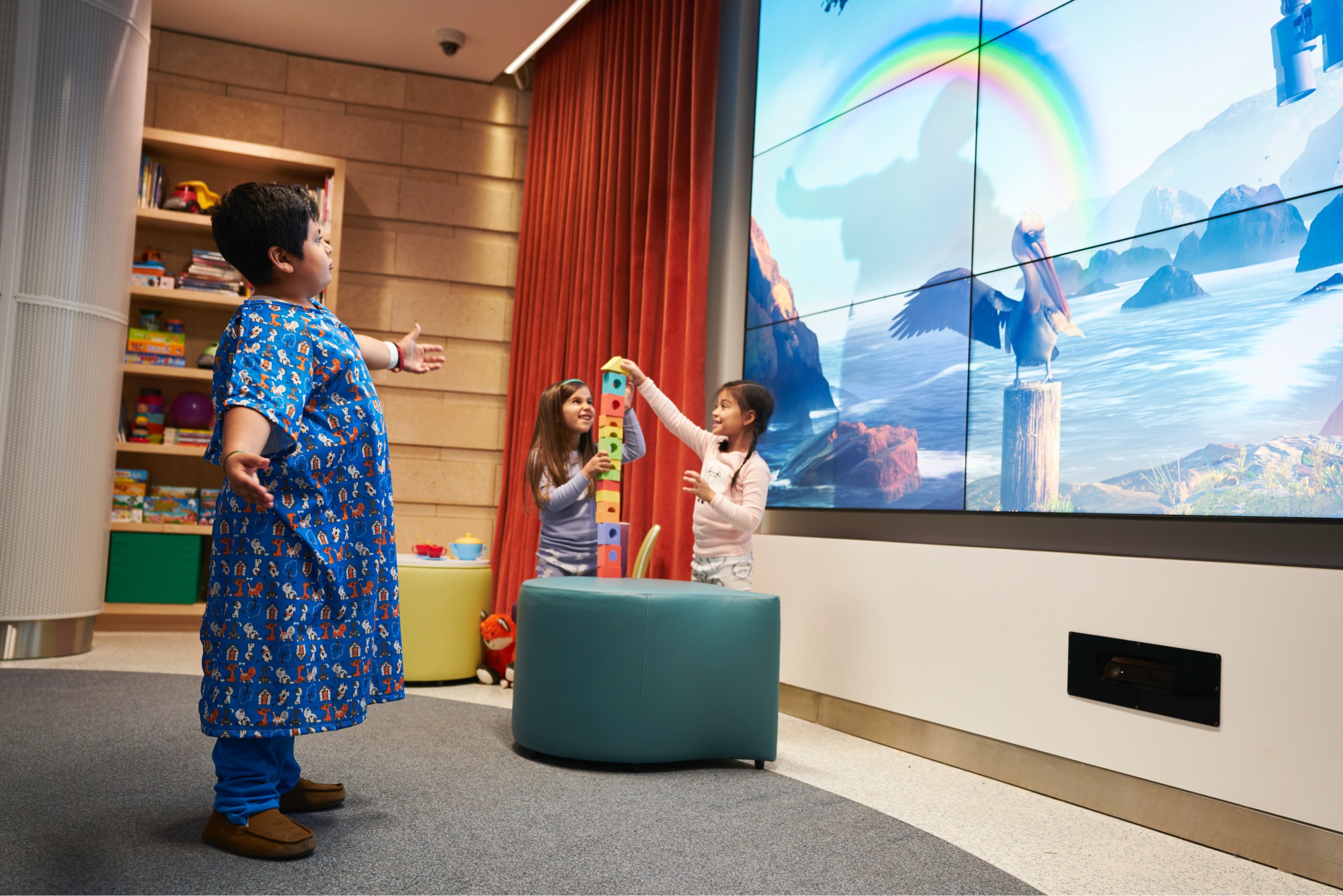 A kid in robe playing with rainbow on interactive video wall at Lucile Packard Children's Hospital at Stanford