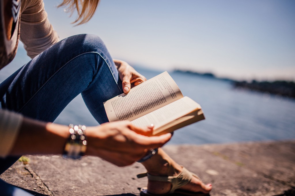 Girl reading book near water