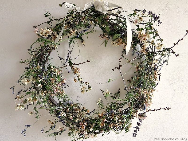 A rustic wreath of dried flowers tied with a lace bow on a white dorm room wall