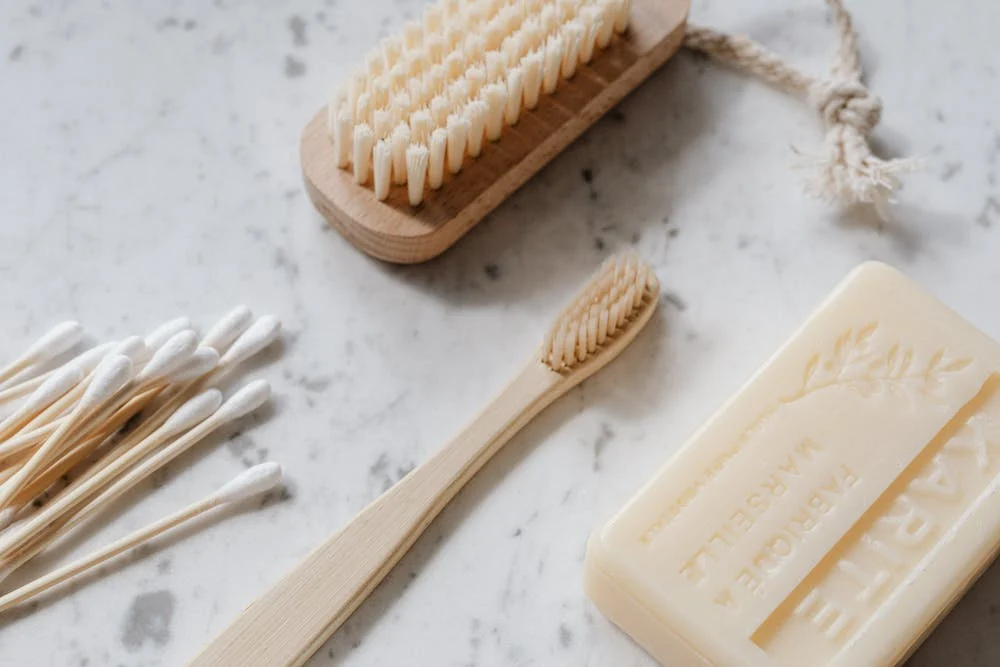 An image of a wooden toothbrush, brush, bar of soap, and several Q-tips on top of a counter.