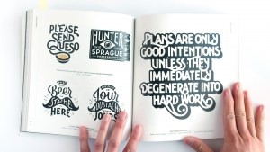 Artist's hand holding a brush pen, working on a detailed lettering project.