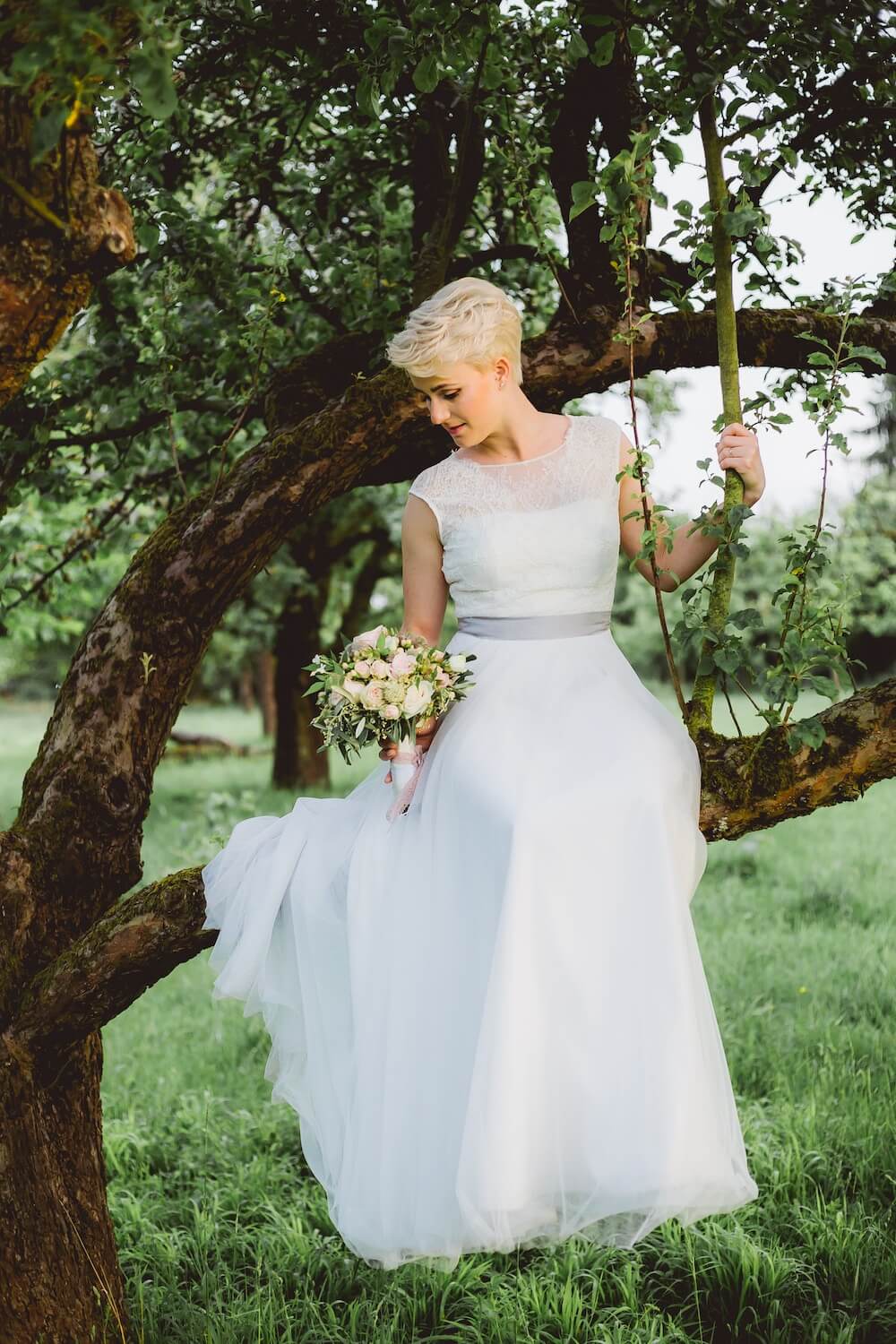 Woman sitting in tree wearing wedding dress