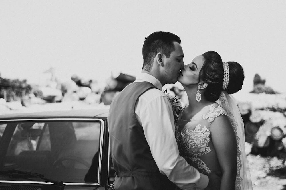 Woman and man standing next to car kissing