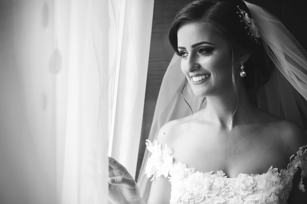 Woman wearing wedding dress pulling curtain open