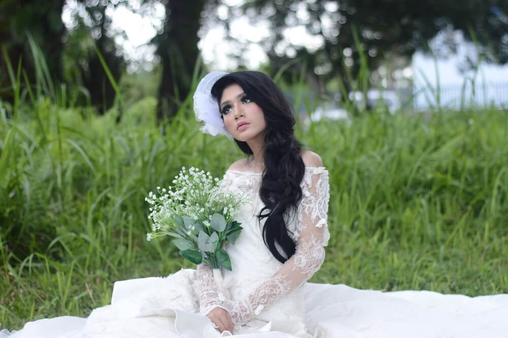 Woman wearing white wedding dress sitting in grass