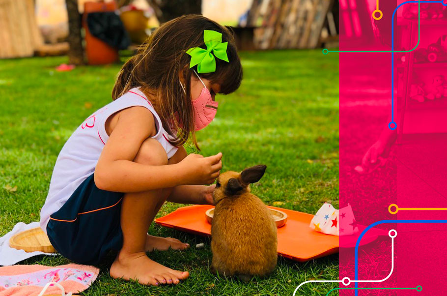 Aluna do Colégio Criando Asas brincando com um coelho no jardim da escola