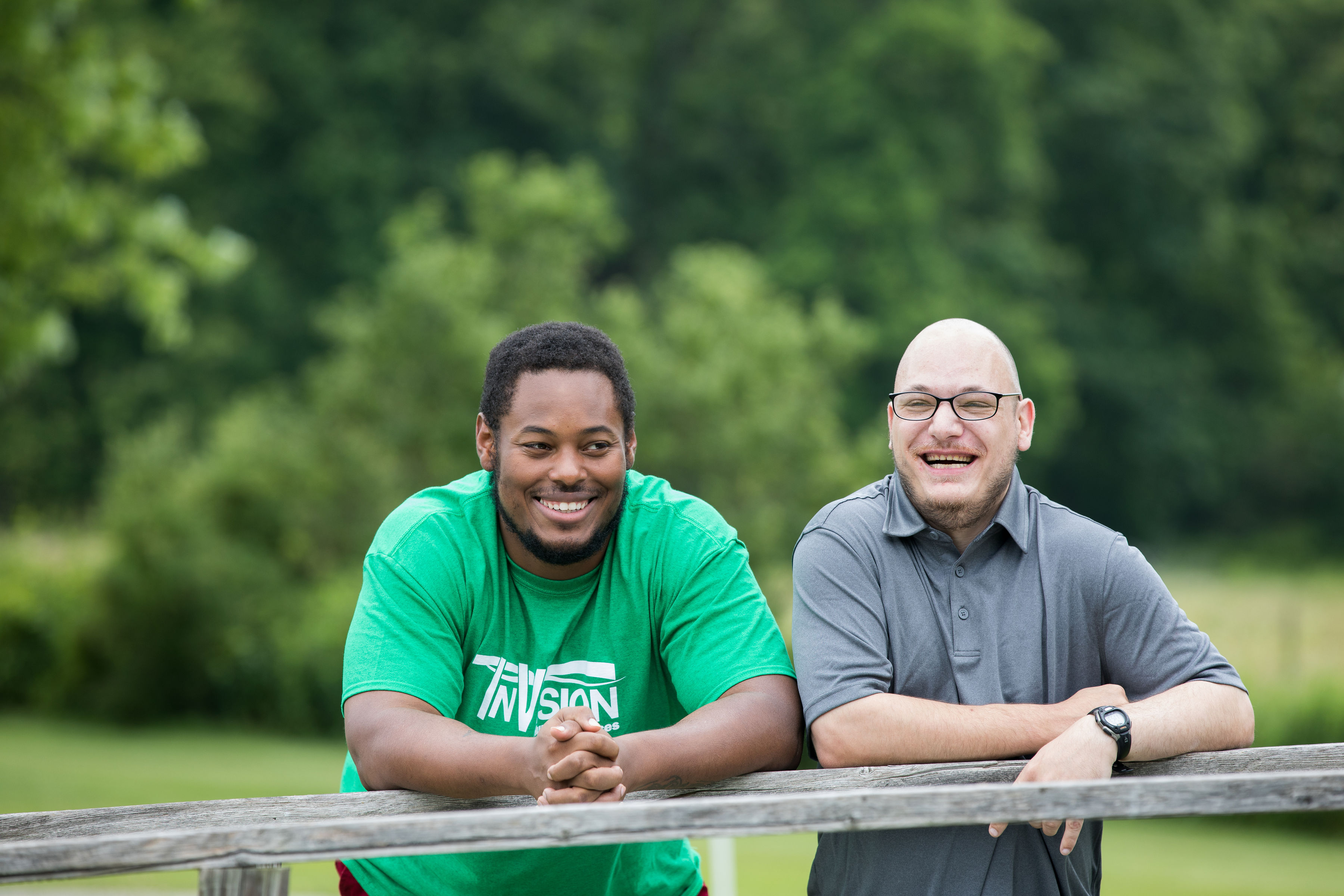 two smiling people leaning their arms on a fence