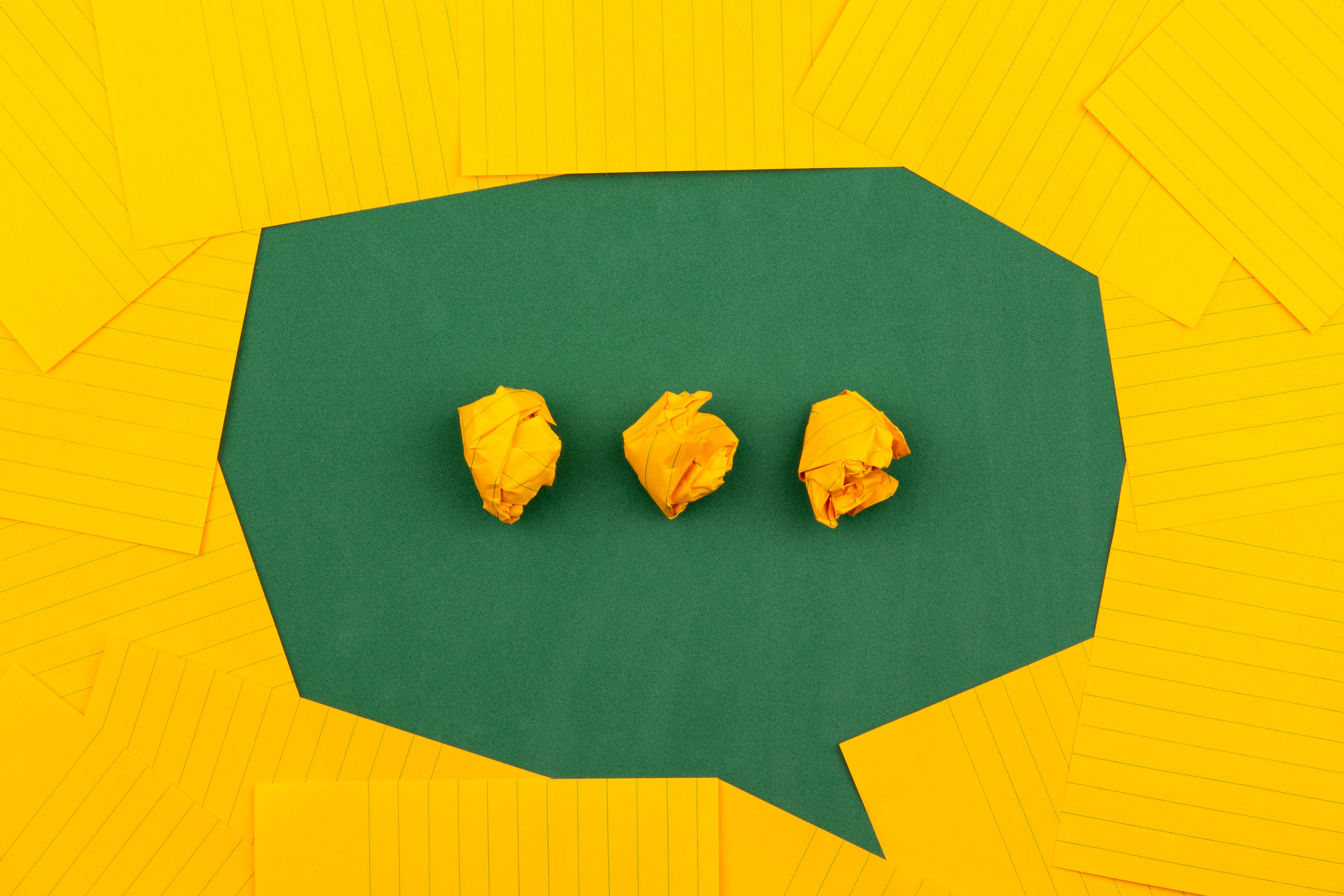 yellow paper surrounding three crumpled pieces of yellow paper in a row outlining a thought bubble